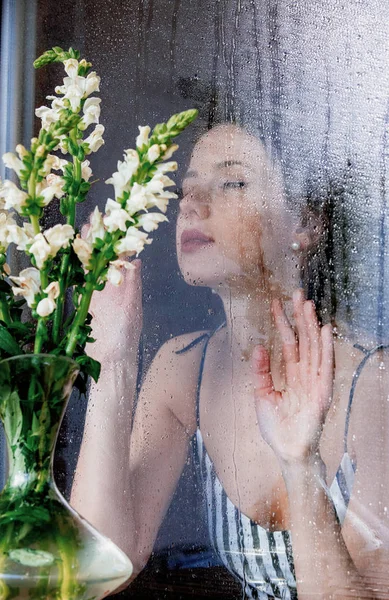 雨后坐在潮湿的窗前的年轻而悲伤的女人错过了这个计划 — 图库照片