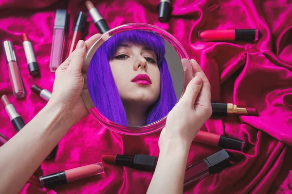 Jovem mulher com cabelo roxo olhando em um espelho com cosméticos — Fotografia de Stock