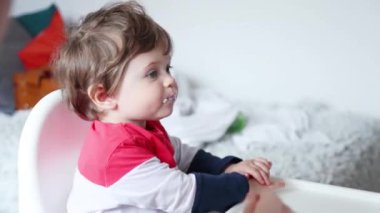 Evde beslenme sırasında bir sandalyede oturan küçük yürümeye başlayan çocuk.