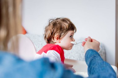 anne t öğle yemeği sırasında bir kaşık ile küçük bir yürümeye başlayan çocuk besler