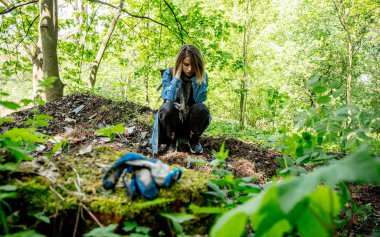 Ormanda çöpün yanında sırt çantalı bir kadın.