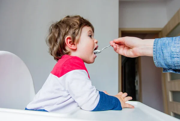 Madre nutre un piccolo bambino ragazzo con un cucchiaio durante il pranzo in t — Foto Stock