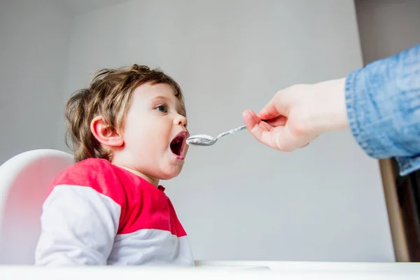 Madre nutre un piccolo bambino ragazzo con un cucchiaio durante il pranzo in t — Foto Stock