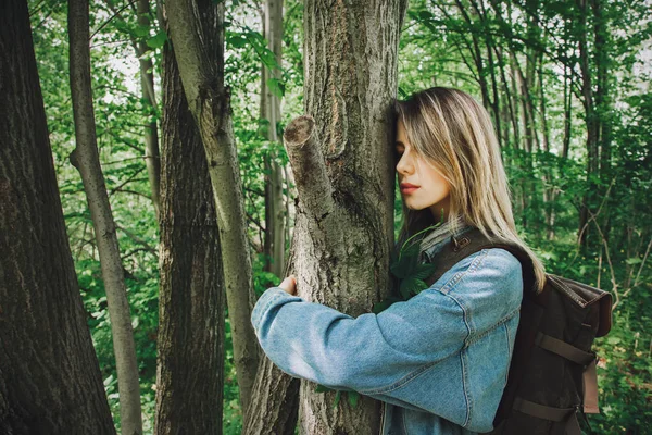 Vrouw met rugzak knuffelen een boom in bos — Stockfoto