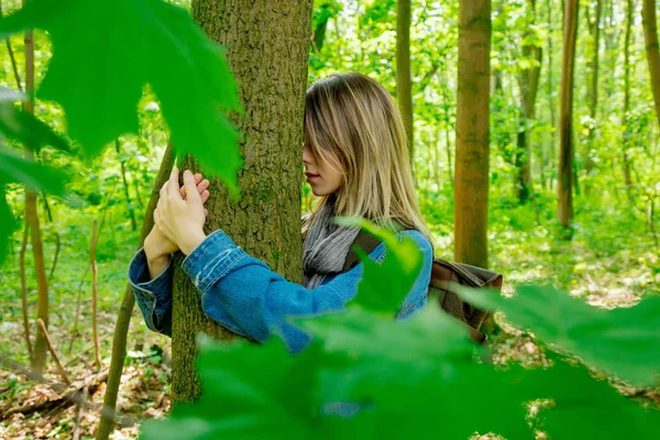 Женщина с рюкзаком обнимает дерево в лесу — стоковое фото