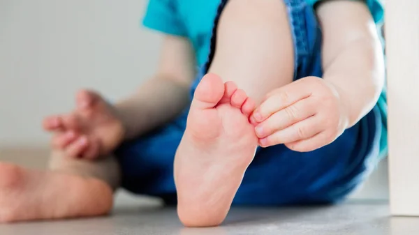 Niño pequeño se sienta en el suelo y sostiene su pie — Foto de Stock