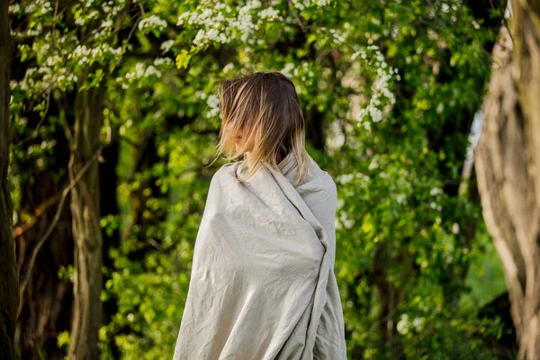 A young girl wrapped in a blanket is standing in a meadow near t — Stock Photo, Image