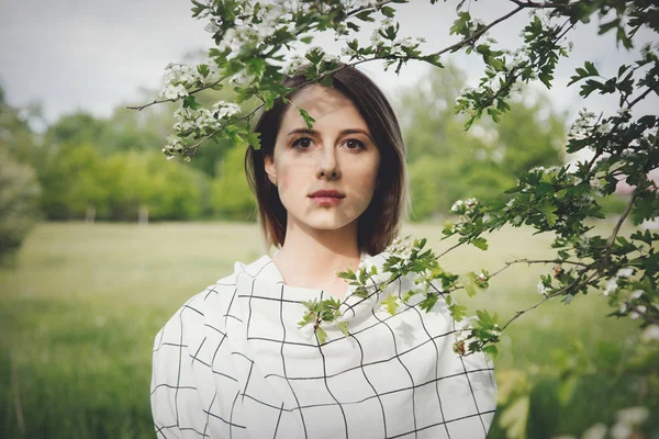 Jovem mulher em uma dressstay xadrez perto de uma árvore de floração — Fotografia de Stock