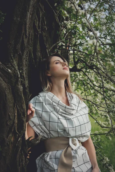 Ung kvinna i rutig klänning bo nära ett blommande träd — Stockfoto