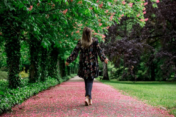 Woman walking down barefoot at alley with blossom trees in sprin — ストック写真