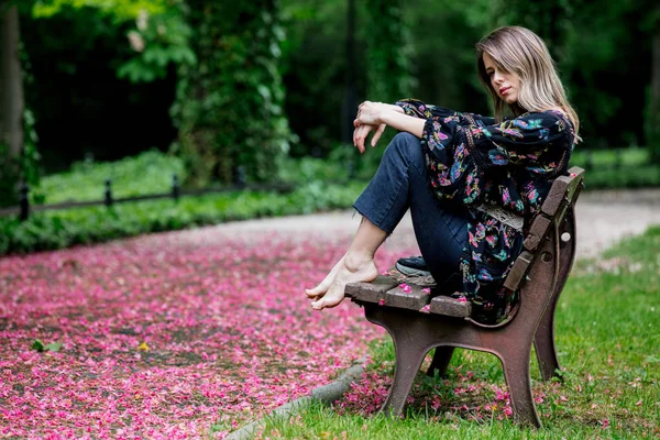 Barfota kvinna sitter på en bänk i gränd med blom träd — Stockfoto