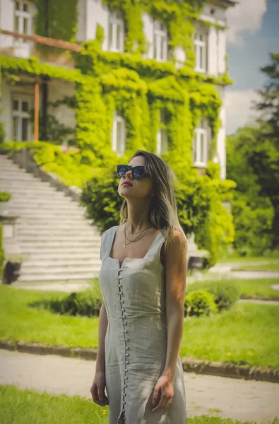 Νεαρή γυναίκα με φόρεμα και γυαλιά ηλίου με παλιό κτίριο σε backgro — Φωτογραφία Αρχείου
