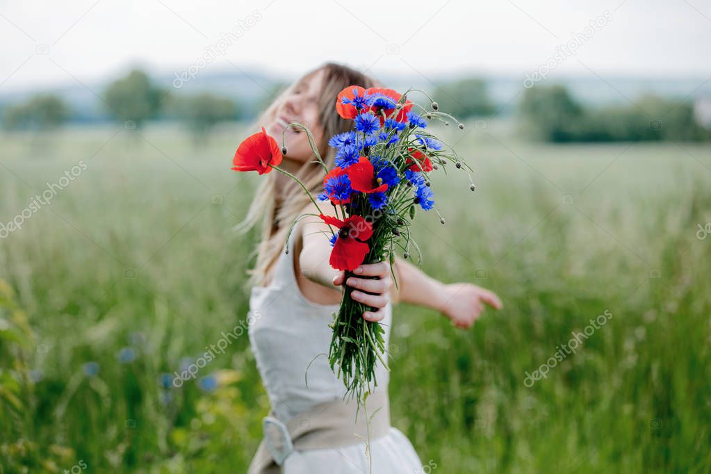 Young woman in dress stay near field with bouquet of Centaurea and Poppy flowers