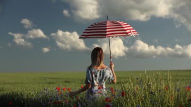 Yeşil buğday tarlasında şemsiyesi olan şapkalı genç kız ve arka planda dağlar.