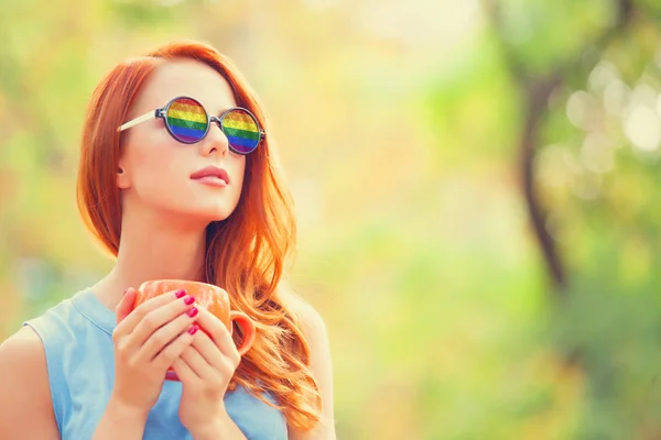 Redhead meisje in zonnebril met regenboog en met kopje — Stockfoto