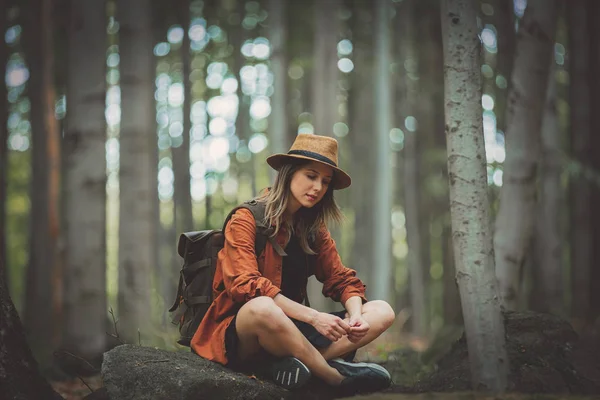 Стильная девушка с рюкзаком, сидящая в камне летом — стоковое фото