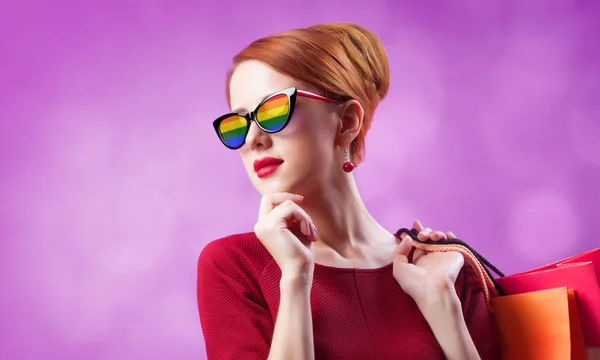 Redhead vrouw in zonnebril met regenboog en met boodschappentassen — Stockfoto