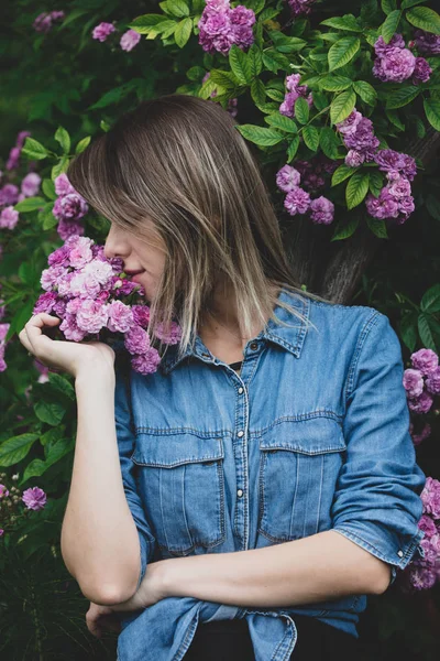 Jovem mulher perto de arbusto de flores roxas em um jardim — Fotografia de Stock