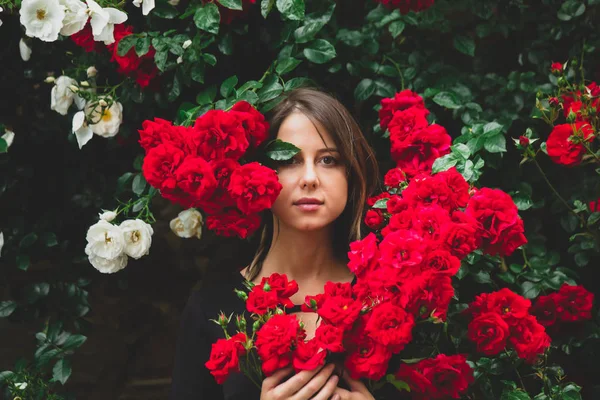 Mladá dívka poblíž keře červených a bílých růží — Stock fotografie