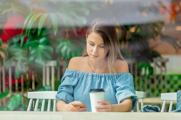 Young woman in a cafe and drinking coffee and use mobile phone w — Stock Photo, Image