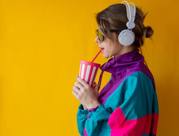 Mujer joven en ropa de estilo 90 con taza y auriculares —  Fotos de Stock