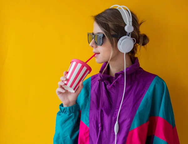 Mujer joven en ropa de estilo 90 con taza y auriculares —  Fotos de Stock