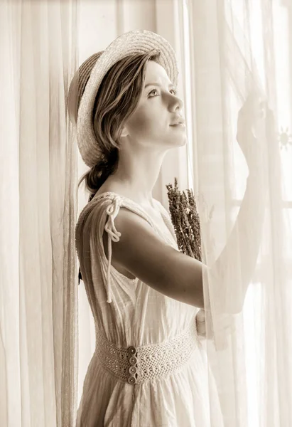 Kobieta w białej sukni, trzymając lawendy w pobliżu okna — Zdjęcie stockowe