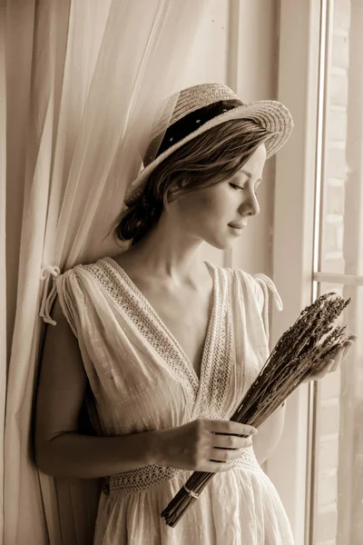 Mujer en vestido blanco sosteniendo lavanda cerca de la ventana —  Fotos de Stock