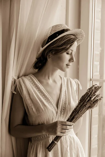 Woman in white dress holding lavender near window — Stock Photo, Image