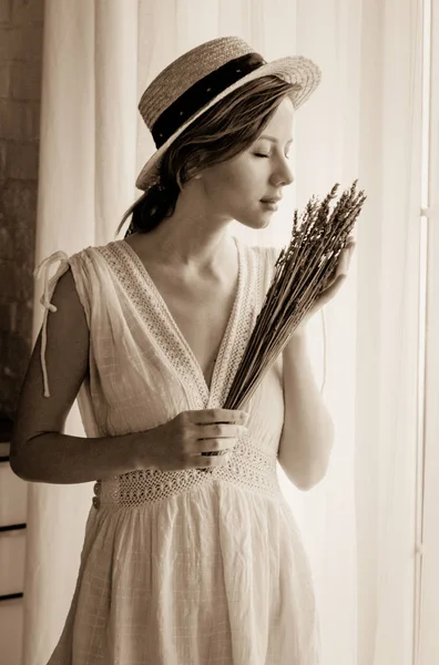 Kvinna i vit klänning holding lavendel nära fönster — Stockfoto