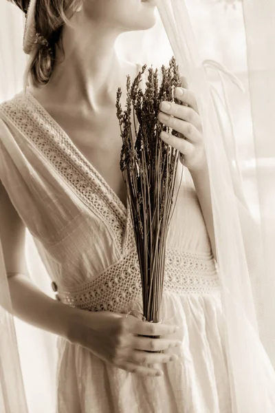 Mulher de vestido branco segurando lavanda perto da janela — Fotografia de Stock