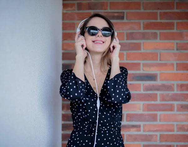 Kvinna med hörlurar och solglasögon på tegelvägg bakgrund — Stockfoto