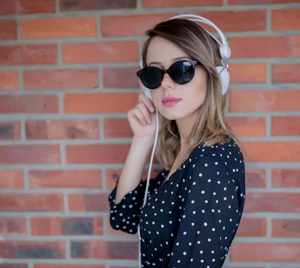 Vrouw met koptelefoon en zonnebril op bakstenen muur achtergrond — Stockfoto