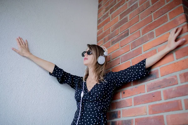 Mulher com fones de ouvido e óculos de sol no fundo da parede de tijolo — Fotografia de Stock