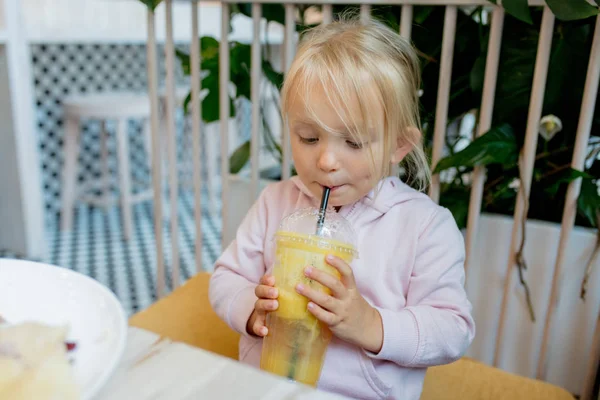 Маленькая девочка пьет апельсиновый сок в кафе — стоковое фото