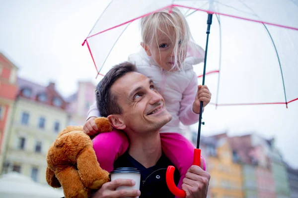 Menina com guarda-chuva senta-se em seus ombros pais — Fotografia de Stock