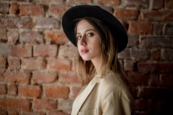 Chica de estilo en sombrero y ropa sobre un fondo de pared de ladrillo —  Fotos de Stock