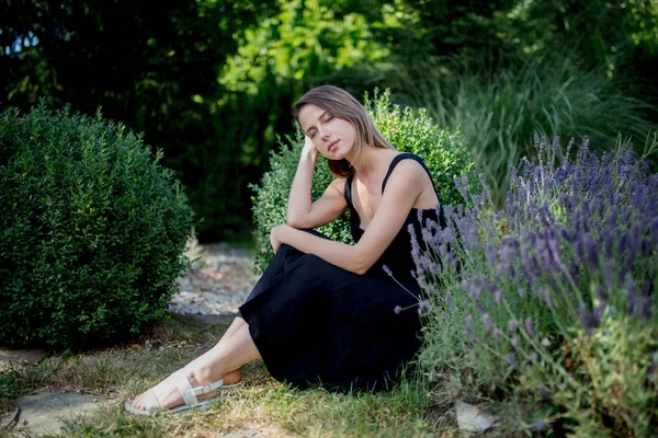Jeune femme en robe sombre assise près des fleurs de lavande — Photo