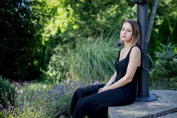 Jonge vrouw in donkere jurk zittend in de buurt van lavendel bloemen — Stockfoto