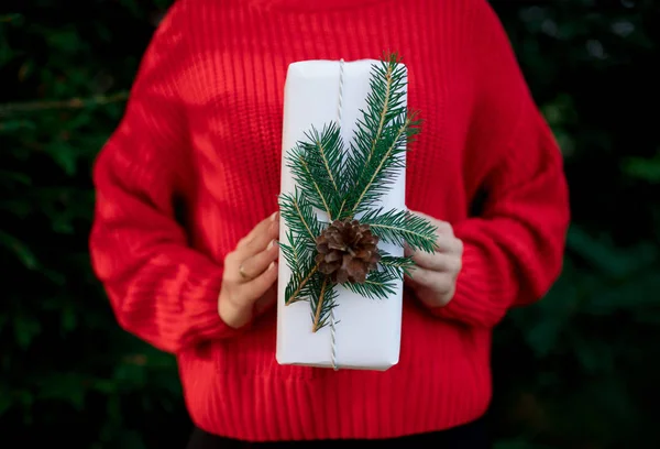Жінка в червоному светрі з різдвяним подарунком біля соснового дерева — стокове фото