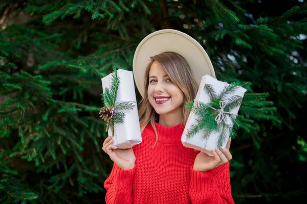 Woman in red sweater with christmas gifts near pine tree — Stock Photo, Image