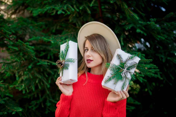 松の木の近くにクリスマスプレゼントと赤いセーターの女性 — ストック写真