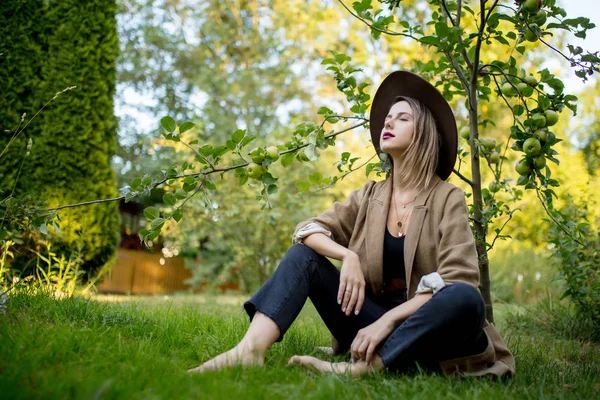 Kvinna har en koppla av i en trädgård nära unga äppelträd — Stockfoto