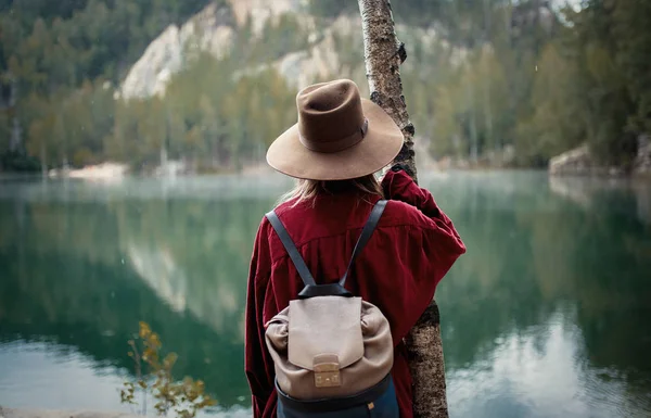 Frau mit Hut und rotem Hemd am See in den Bergen. — Stockfoto