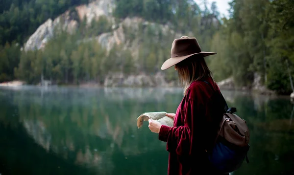 Jovem mulher de chapéu e camisa vermelha com mapa perto do lago — Fotografia de Stock