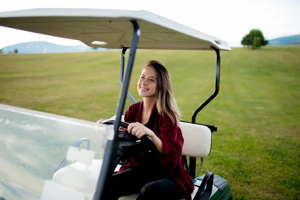 Young woman have a fun with golf buggy car on a field in mountains — Stock Photo, Image