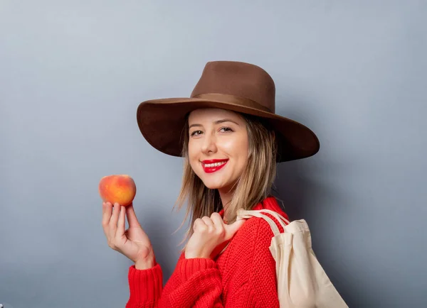 Vrouw in rode trui met perzik en tas — Stockfoto