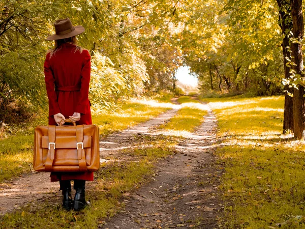 Woman in red coat with suitcase on countryside road — Stock Photo, Image