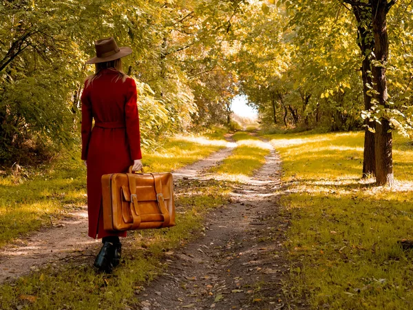 Kvinna i röd rock med resväska på landsväg — Stockfoto