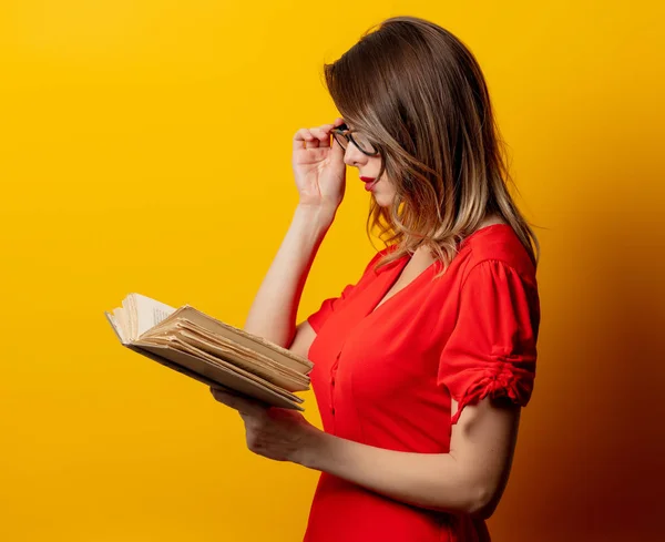 Krásná žena v červených šatech s knihou na žlutém pozadí — Stock fotografie